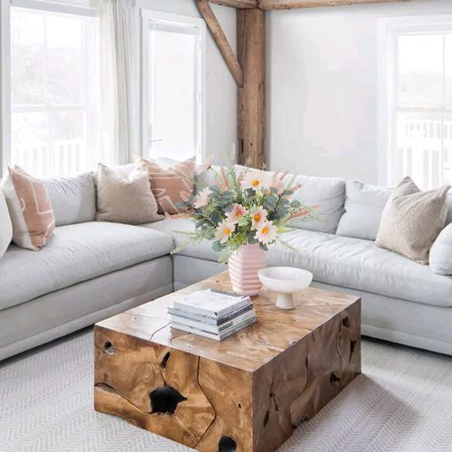 Two artificial wildflower bouquets in a pink vase on a wooden coffee table in a living room setting.
