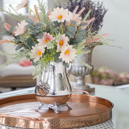 Two artificial wildflower bouquets with pink daisies and eucalyptus in a silver pitcher on a copper tray.