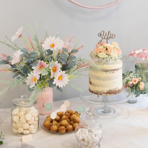 Dessert table with artificial wildflower bouquets, a naked cake, mini muffins, and candies for a baby shower.