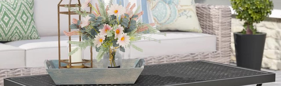 Artificial wildflower bouquet with pink daisies and eucalyptus in a glass vase on a wooden tray on a coffee table