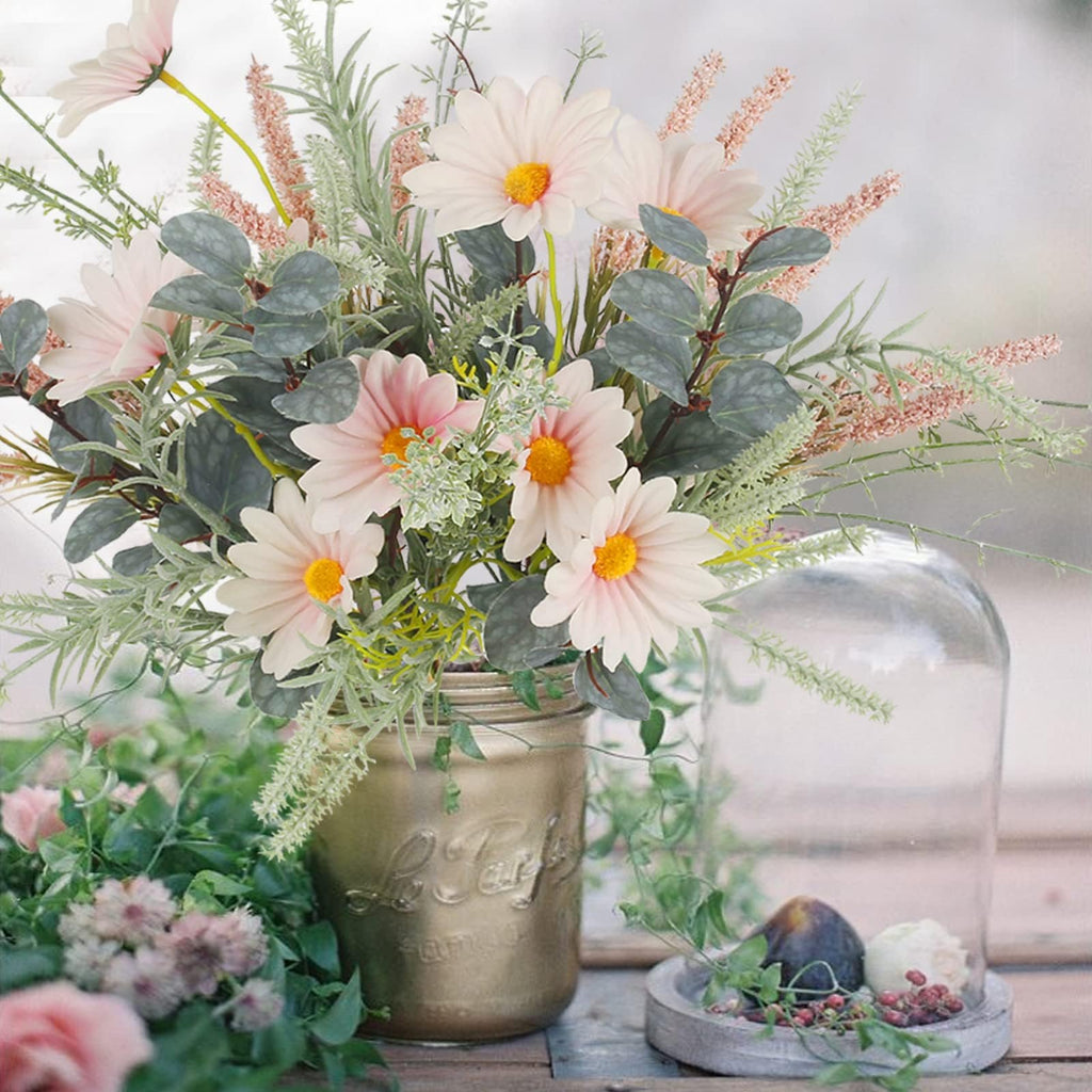 Artificial wildflower bouquet with pink daisies and eucalyptus in a gold mason jar, next to a glass cloche with figs.