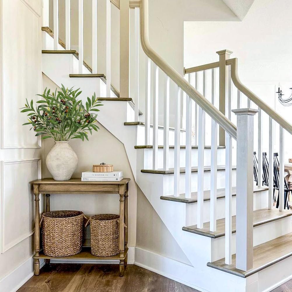 Artificial olive branches with leaves and fruits in a vase on a console table next to a staircase.