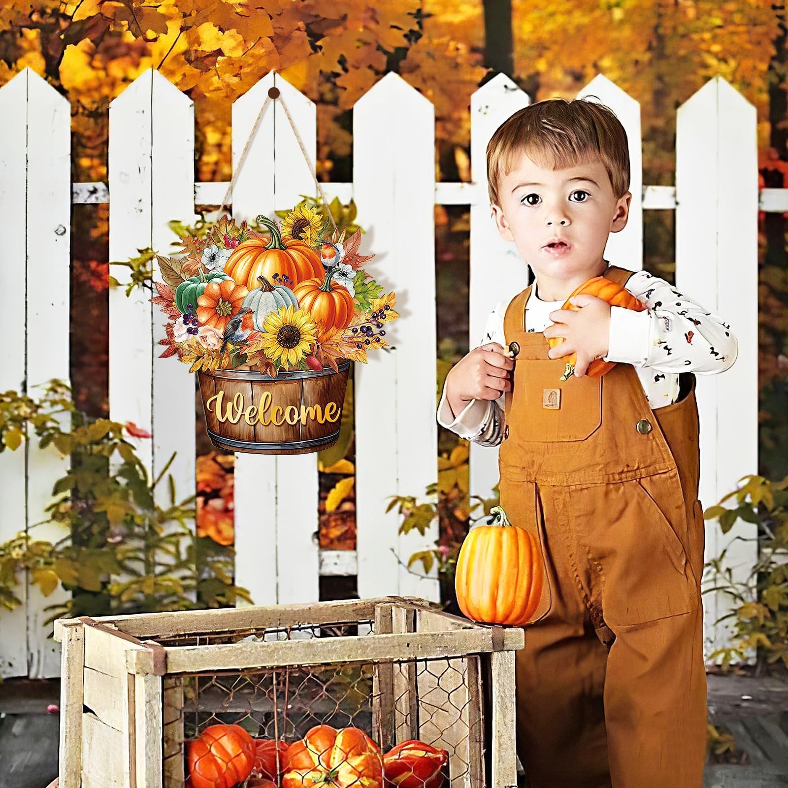 Toddler boy holding pumpkins next to a fall welcome door sign with pumpkins and sunflowers