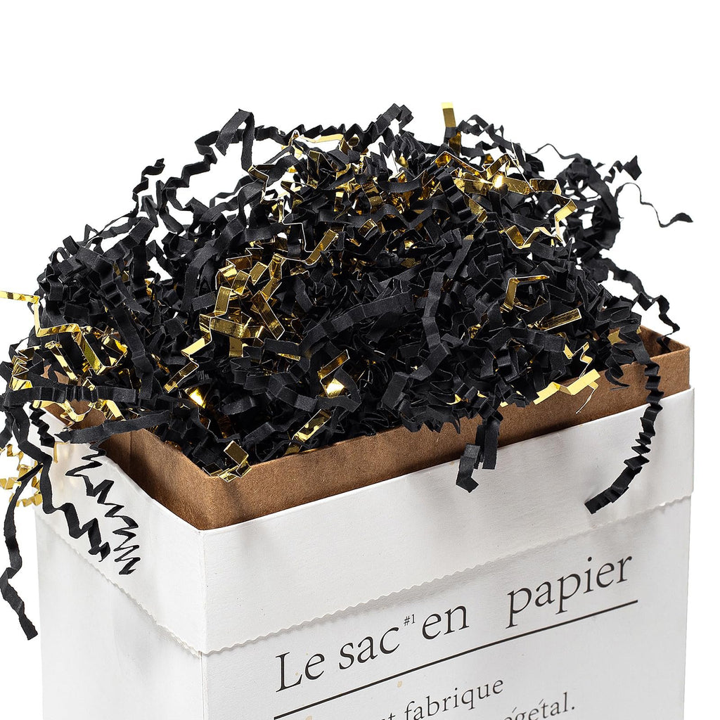 Black and gold crinkle cut paper shred filler overflowing from a white paper gift bag.
