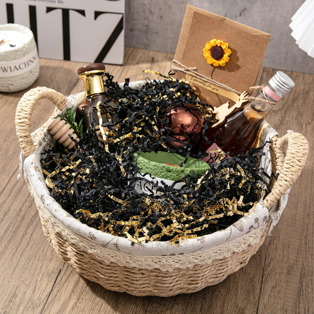 Gift basket filled with black and gold crinkle paper shred, bottles, and decorative items on a wooden surface.