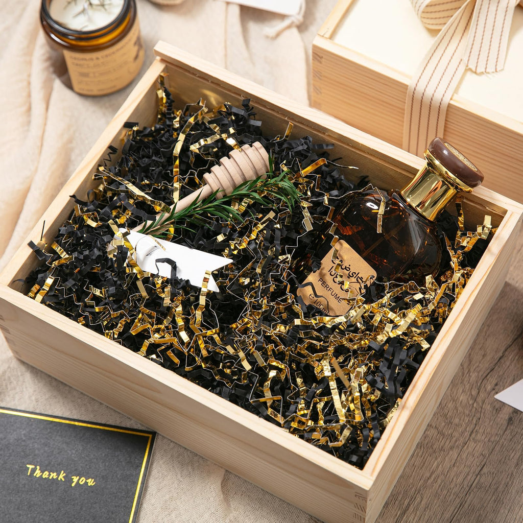 Wooden gift box filled with black and gold crinkle paper shred, a perfume bottle, and a sprig of rosemary.