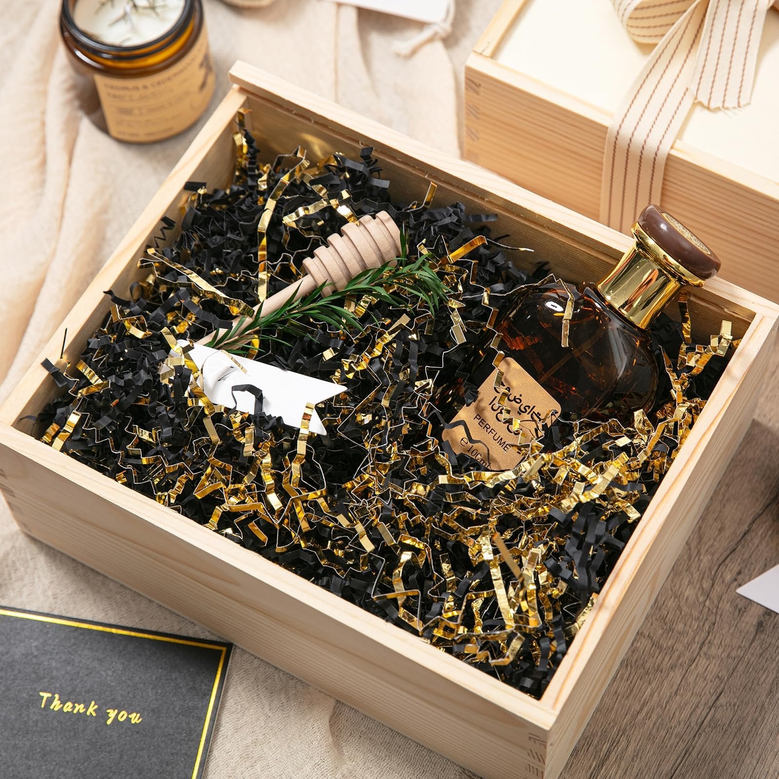 Wooden gift box filled with black and gold crinkle paper shred, a perfume bottle, and a sprig of rosemary.