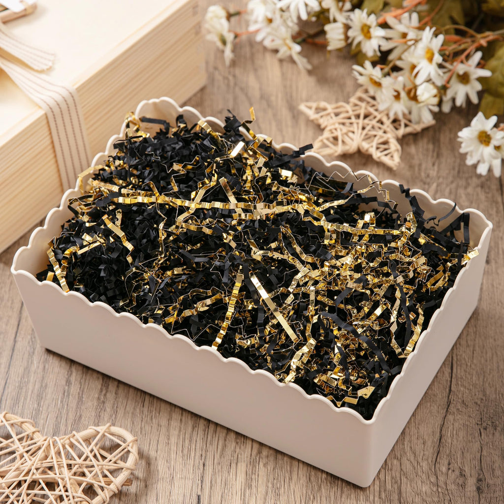 Close-up of black and gold crinkle cut paper shred filler in a decorative white basket on a wooden surface, with decorative elements in the background.