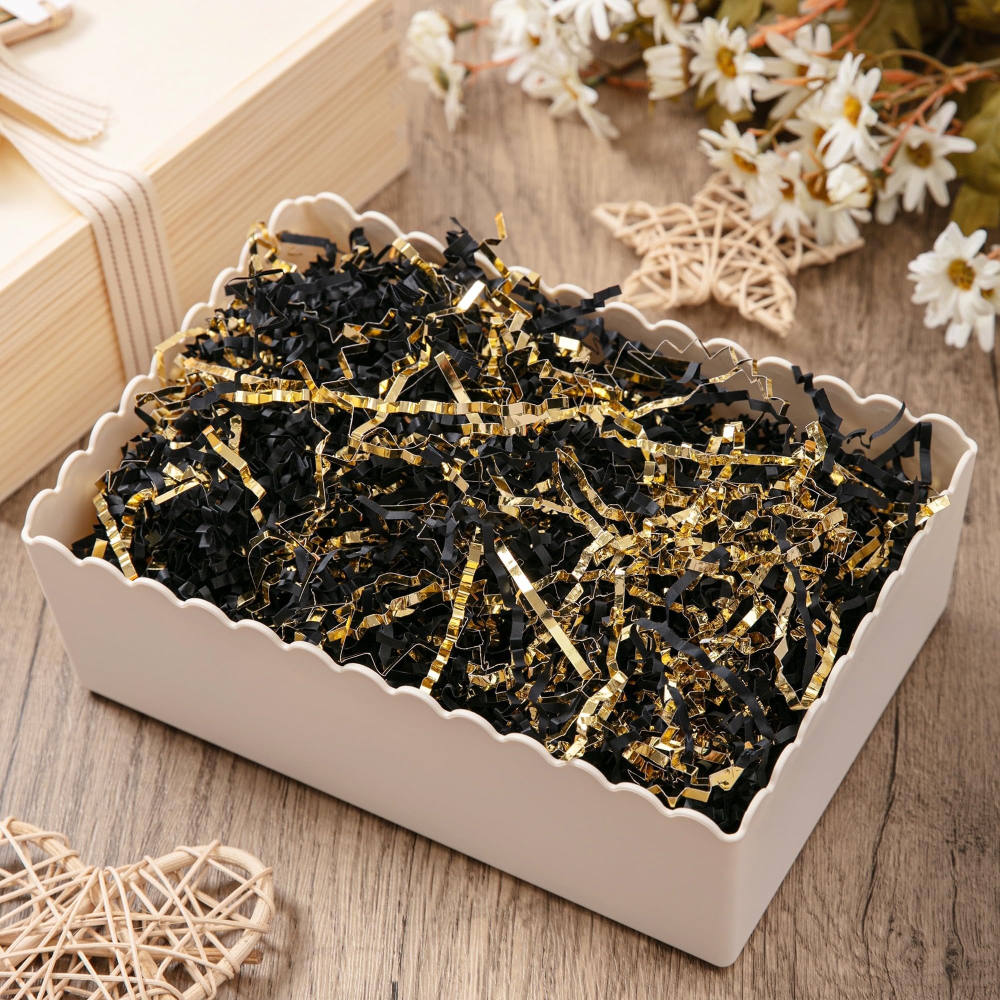 Close-up of black and gold crinkle cut paper shred filler in a decorative white basket on a wooden surface, with decorative elements in the background.