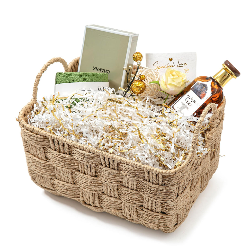 Woven basket filled with white and gold crinkle paper shred, a bottle, a box, and a decorative flower.