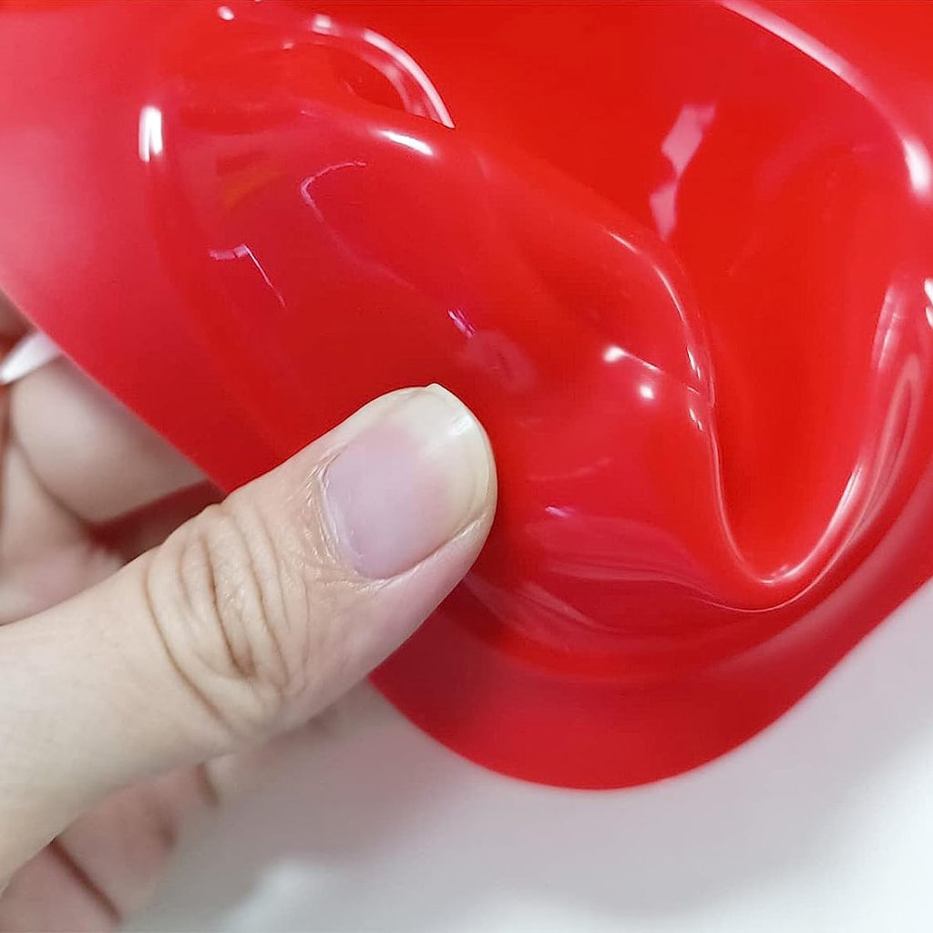 Close-up of a red silicone muffin pan with a finger pressing on the edge. The pan has a non-stick surface.