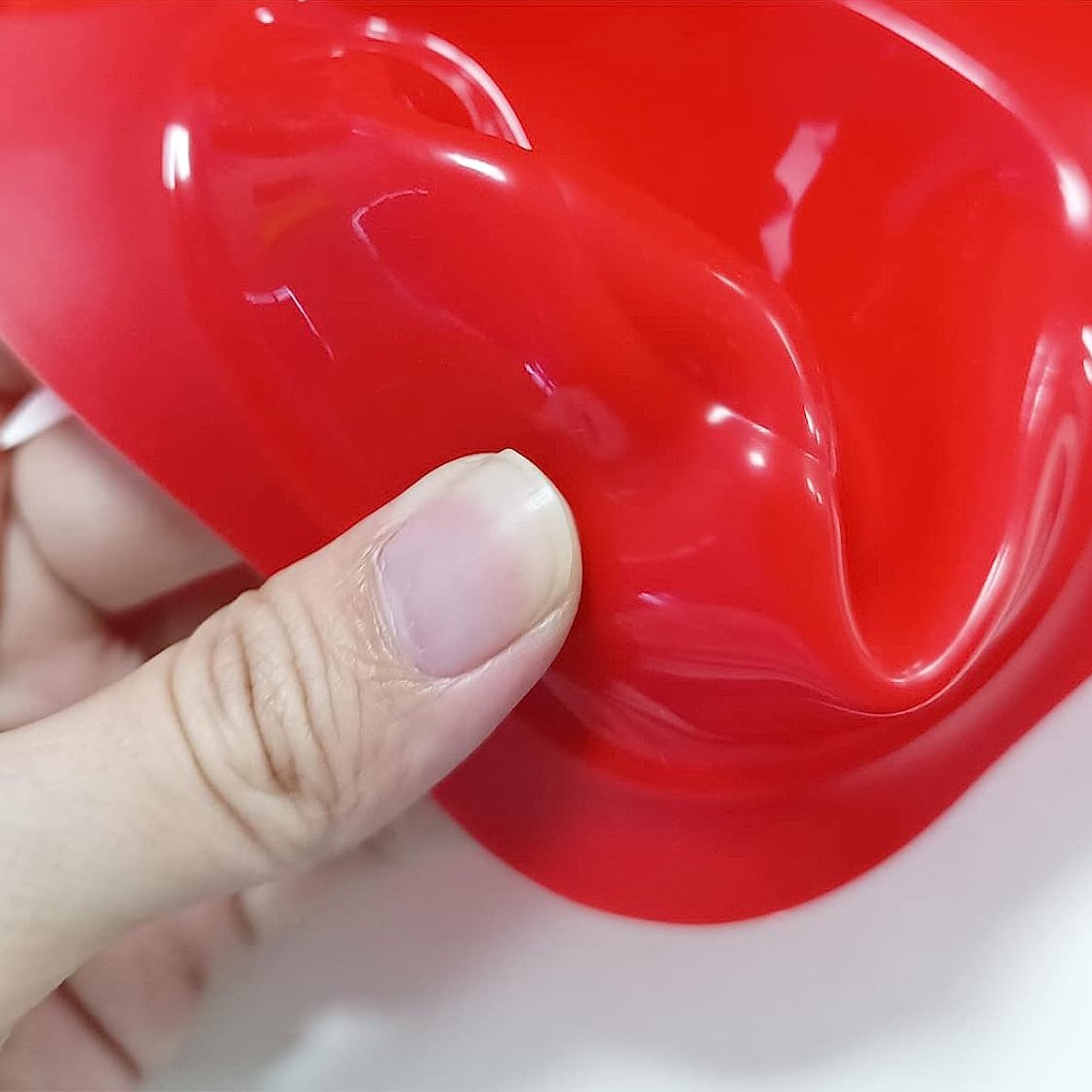 Close-up of a red silicone muffin pan with a finger pressing on the edge. The pan has a non-stick surface.