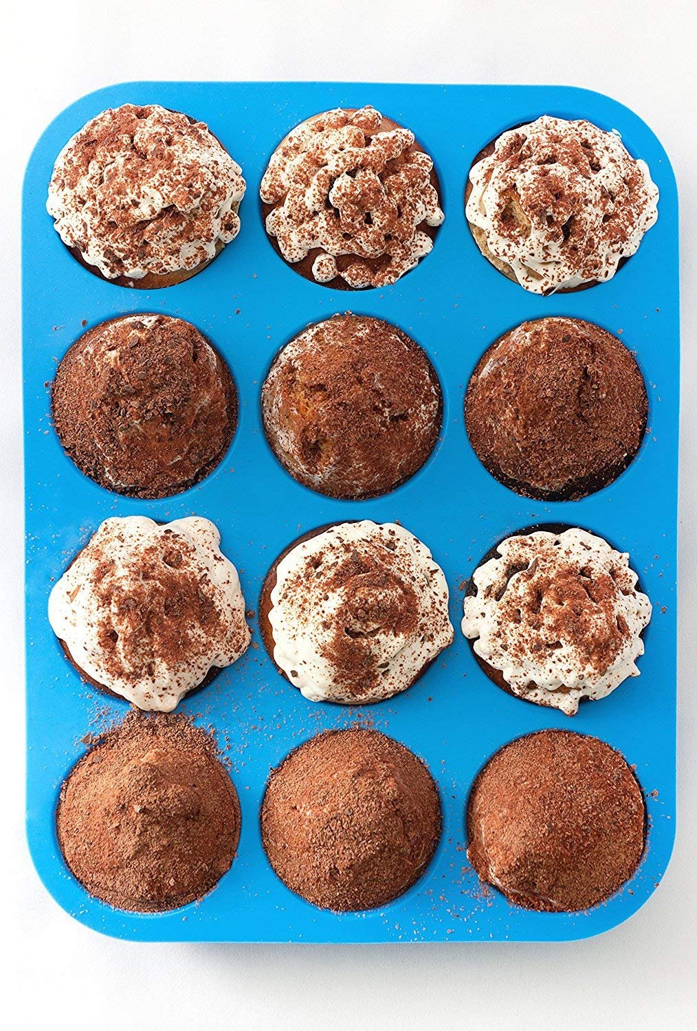 Blue 12-cup silicone muffin pan filled with cupcakes topped with whipped cream and cocoa powder, overhead view.
