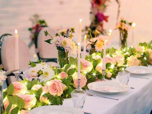 Wedding reception table setting with pink roses, white flowers, candles, and fairy lights.