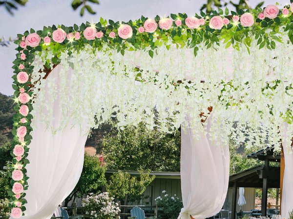 Artificial pink rose and white wisteria floral garland with fairy lights draped over a wedding arch