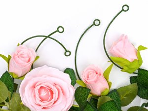 Close-up of pink artificial roses with green leaves and wire stems on a white background.