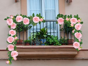 Two pink artificial rose garlands with green leaves draped over a balcony railing with potted plants.