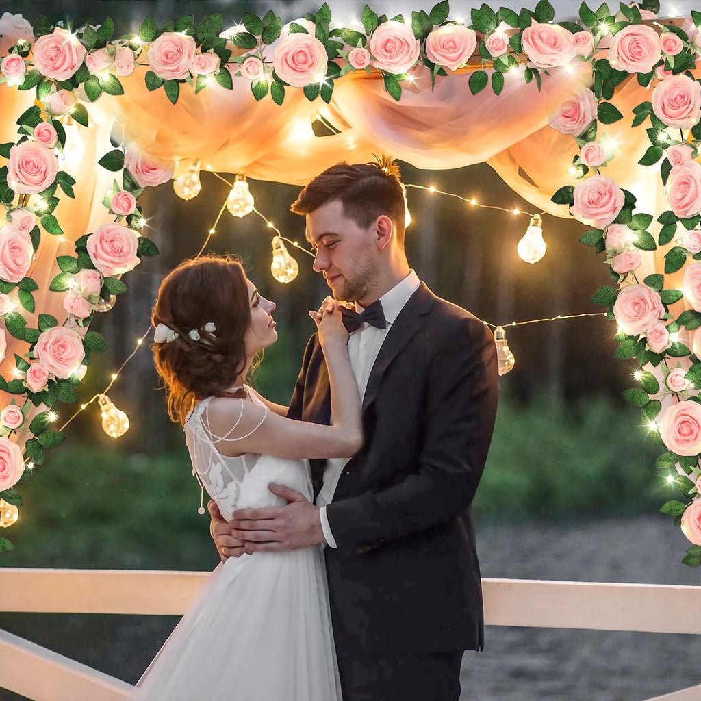 Bride and groom dancing under a wedding arch decorated with pink roses and fairy lights