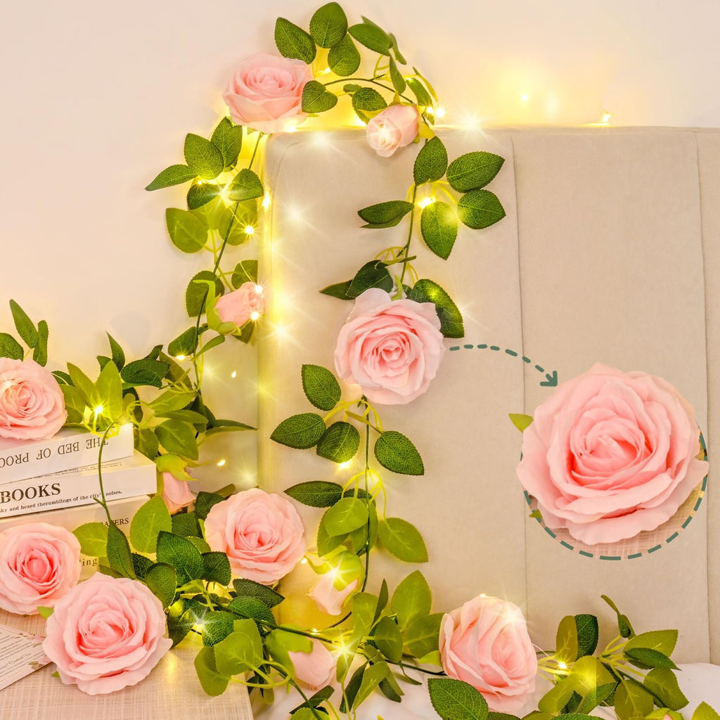 Pink artificial rose garland with green leaves and fairy lights draped over a headboard and books.