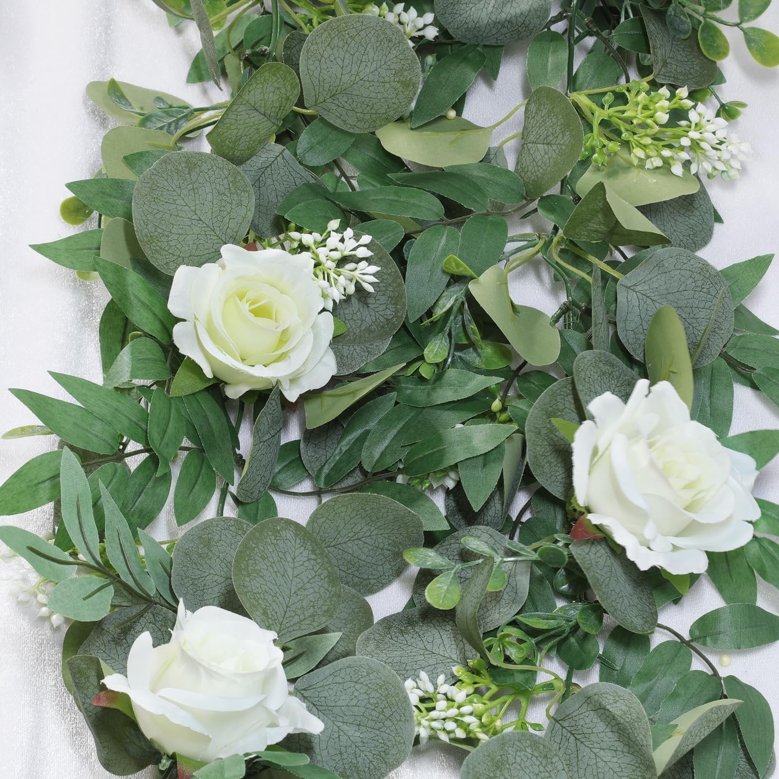 Artificial eucalyptus garland with white roses and small white flowers, close-up view