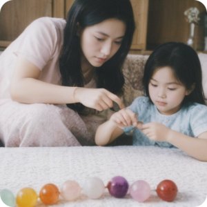 Woman and child sitting on a couch, looking at beads and string for jewelry making.
