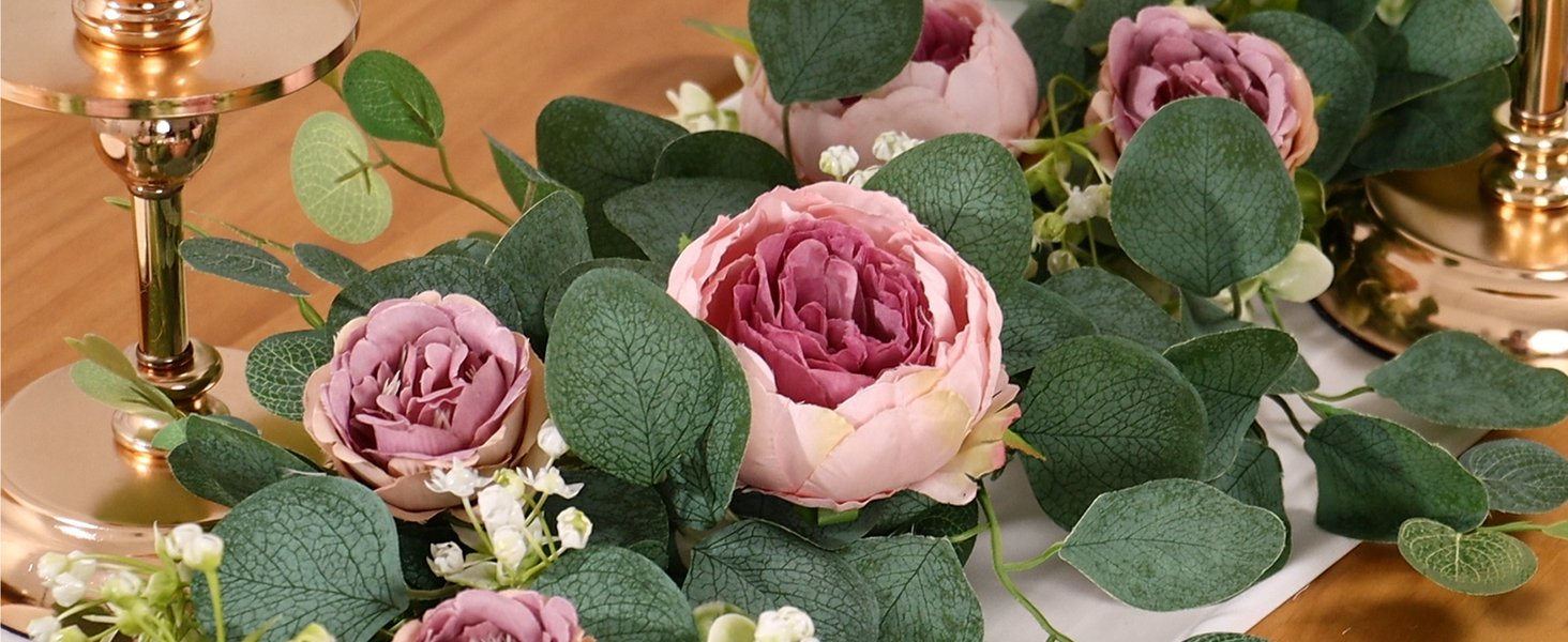 Close-up of vintage pink artificial peony and rose garland with eucalyptus leaves and small white flowers, draped around gold candle holders.