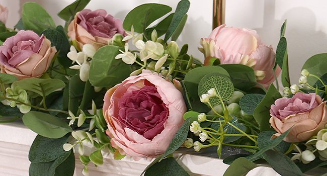 Close-up of artificial peony and rose garland with eucalyptus leaves and small white flowers.