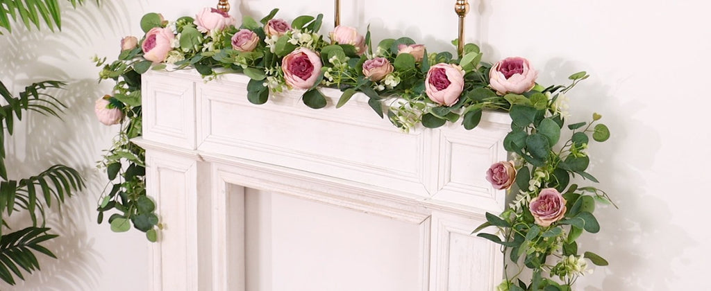 Artificial peony and rose garland with eucalyptus and gypsophila draped over a white mantelpiece.