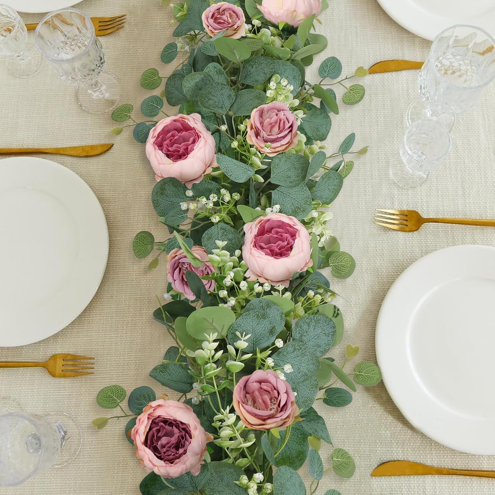 Artificial peony and rose garland with eucalyptus and gypsophila arranged on a table setting with plates and cutlery.