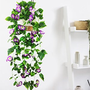 Purple artificial morning glory vine garland with green leaves hanging indoors, with a white shelf and decor in the background.