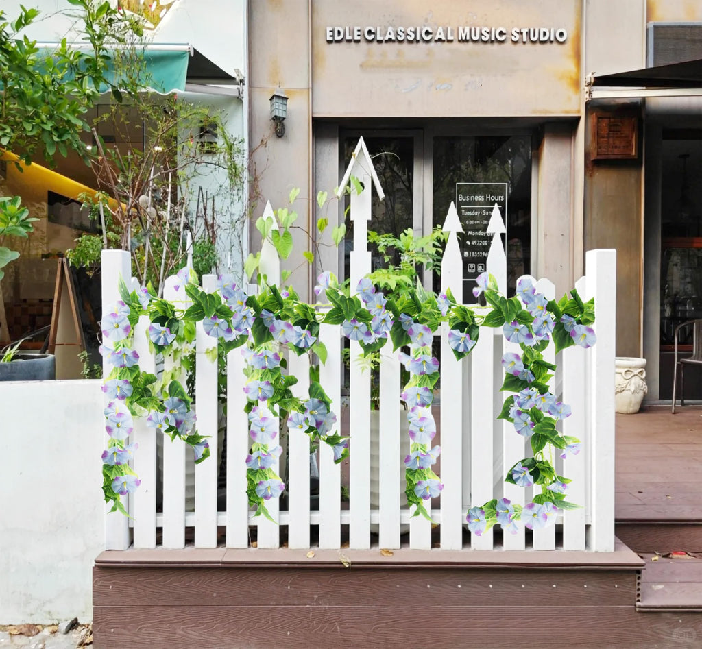 Artificial morning glory vine garland with purple flowers draped on a white picket fence