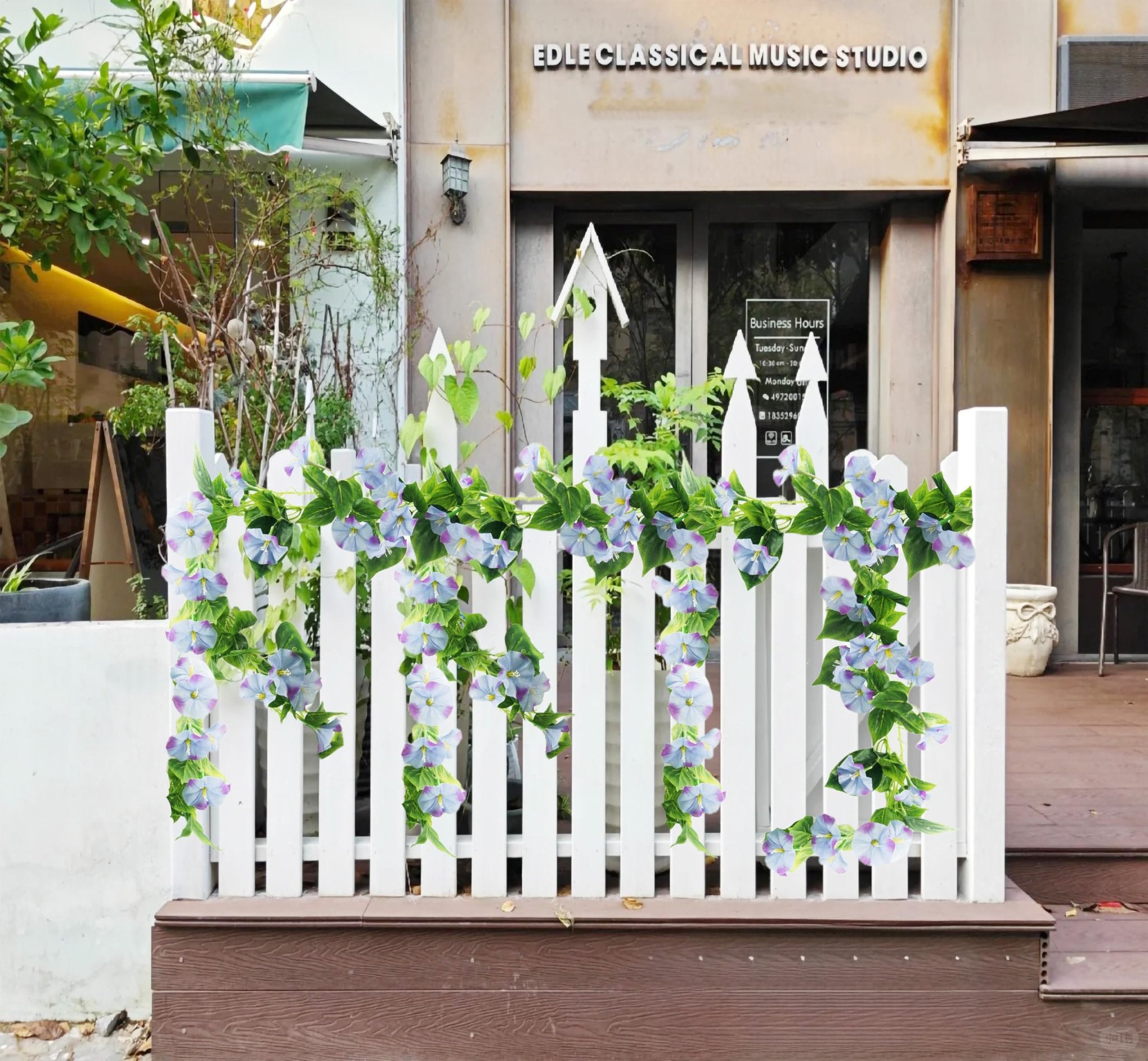 Artificial morning glory vine garland with purple flowers draped on a white picket fence