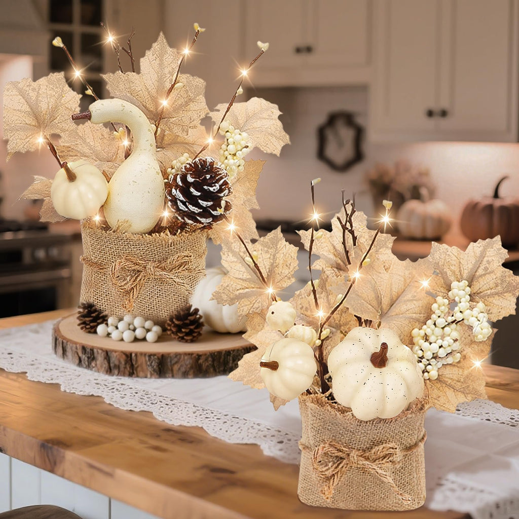Two pre-lit artificial maple trees with pumpkins, pinecones, and berries in burlap pots on a wooden table.