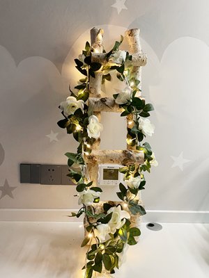 Artificial white rose garland with LED lights draped on a birch ladder against a cloud and star patterned wall