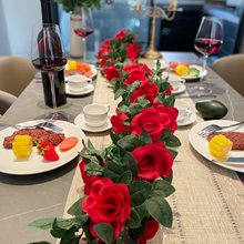 Two artificial red rose garlands draped across a dining table set for a meal, with wine glasses and plates of food.