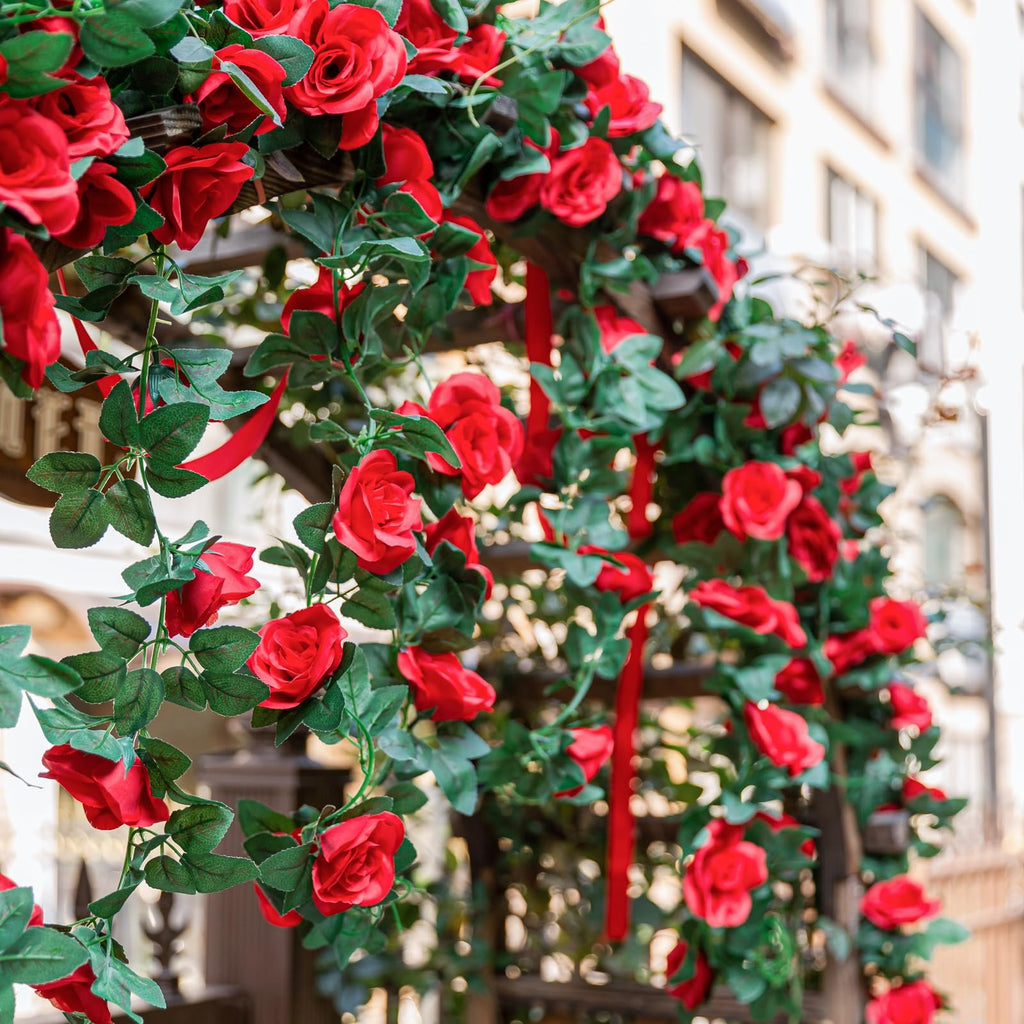 Artificial red rose garland with green leaves draped over a wooden archway, with red ribbons.