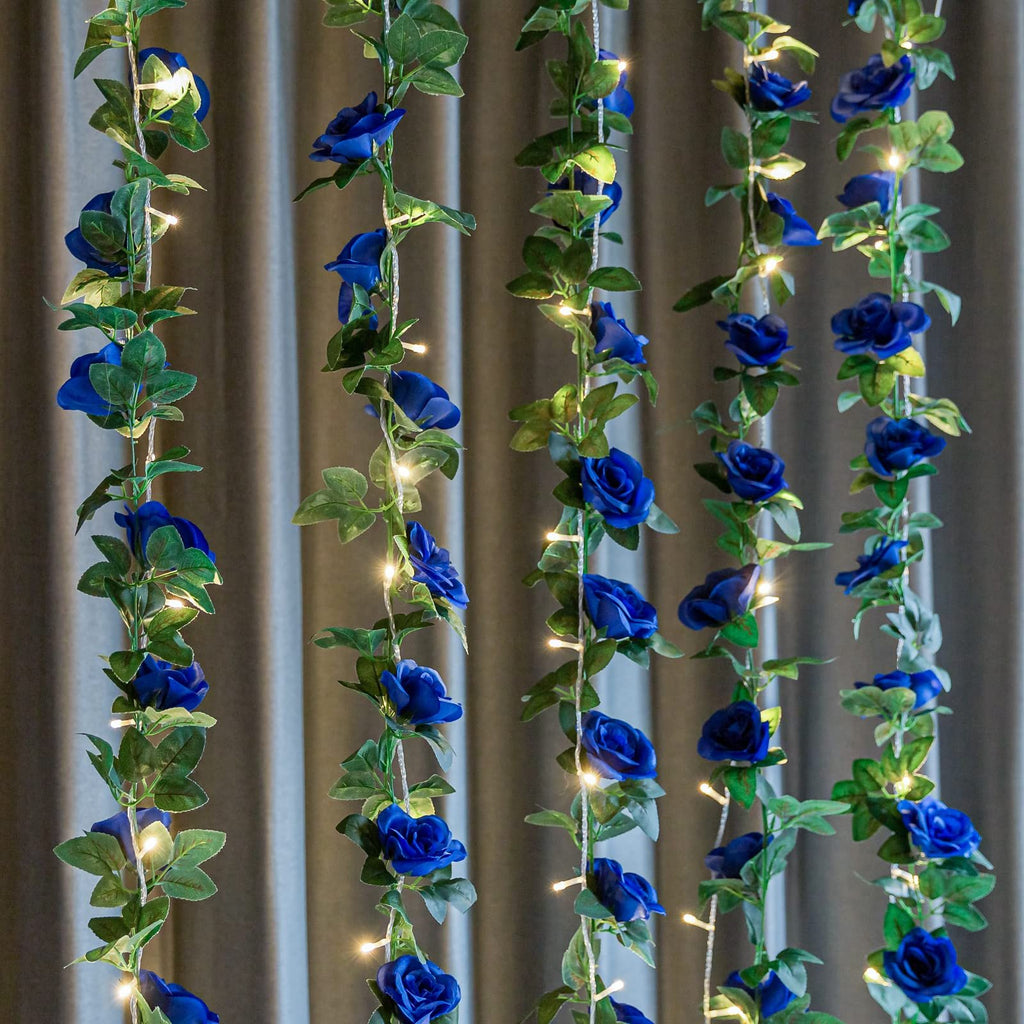 Artificial royal blue rose vine garland with LED lights draped against a curtain background.