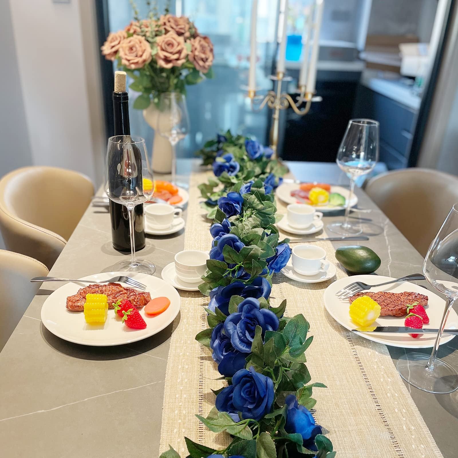 Table setting with blue rose garland, plates of food, wine bottle, and glasses
