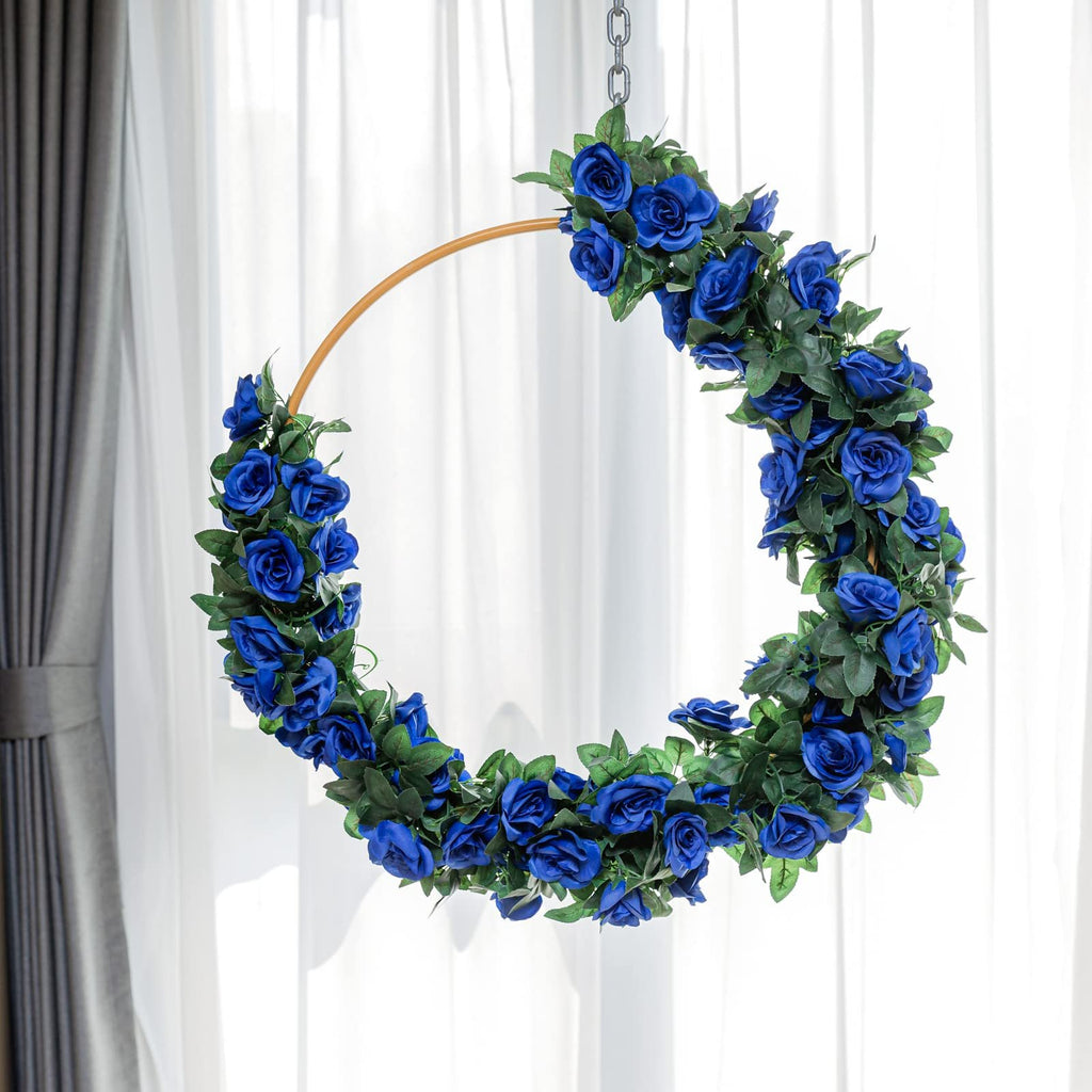 Artificial royal blue rose garland draped on a circular hoop, hanging against a white curtain backdrop.
