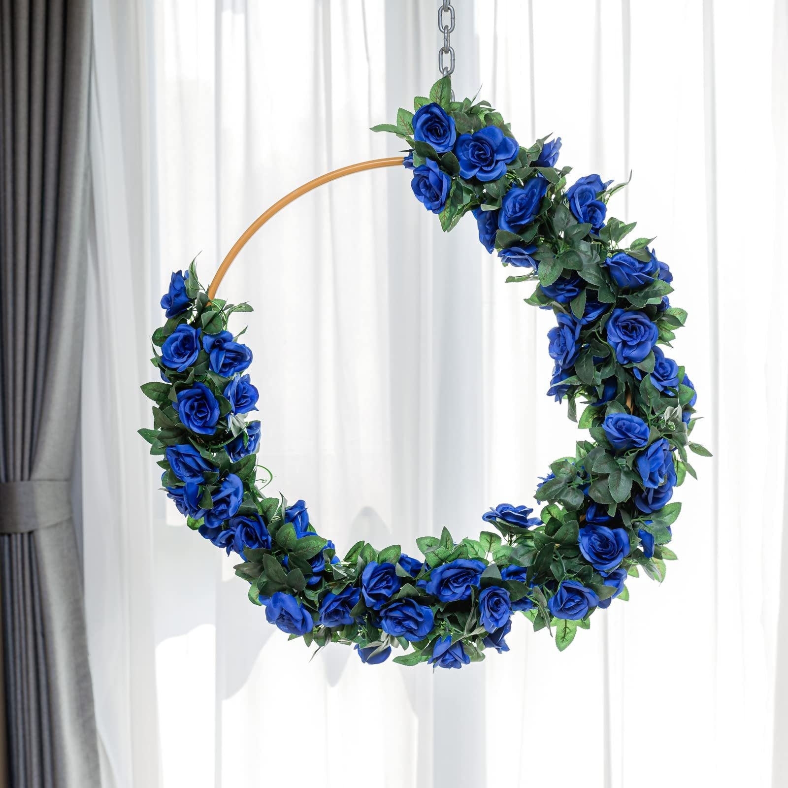 Artificial royal blue rose garland draped on a circular hoop, hanging against a white curtain backdrop.