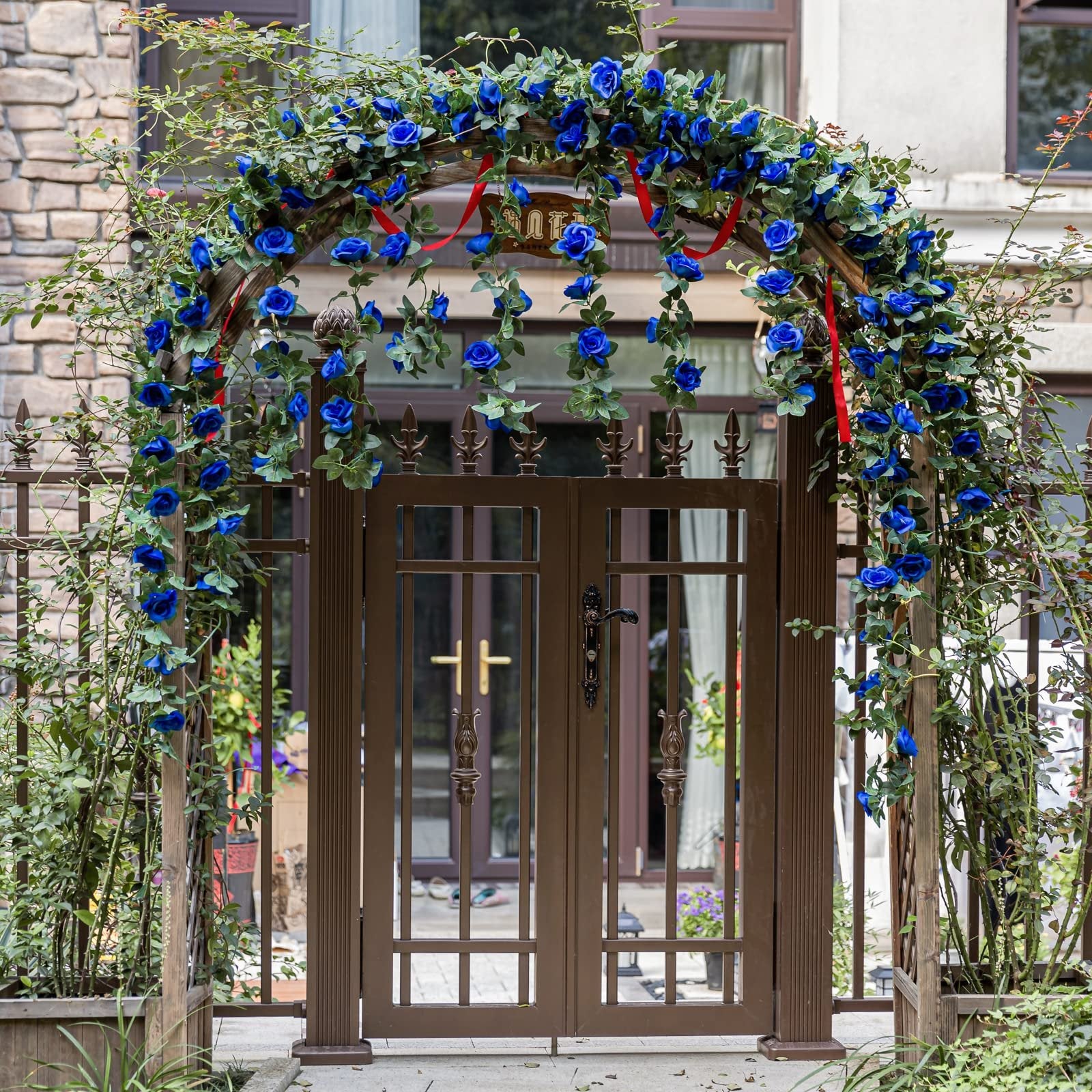 Artificial royal blue rose vine garland draped over a wooden archway and brown metal gate