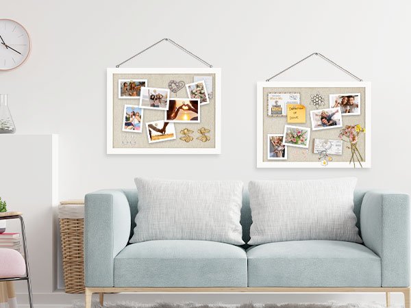 Two white-framed linen cork boards hanging on a wall above a light blue sofa, each displaying photos and decorative items.