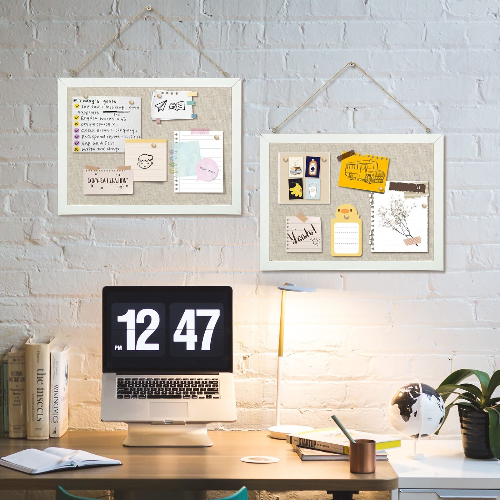 Two linen cork boards with white wood frames hang on a brick wall above a desk with a laptop and lamp. One board displays a to-do list and drawings, the other has various notes and images.