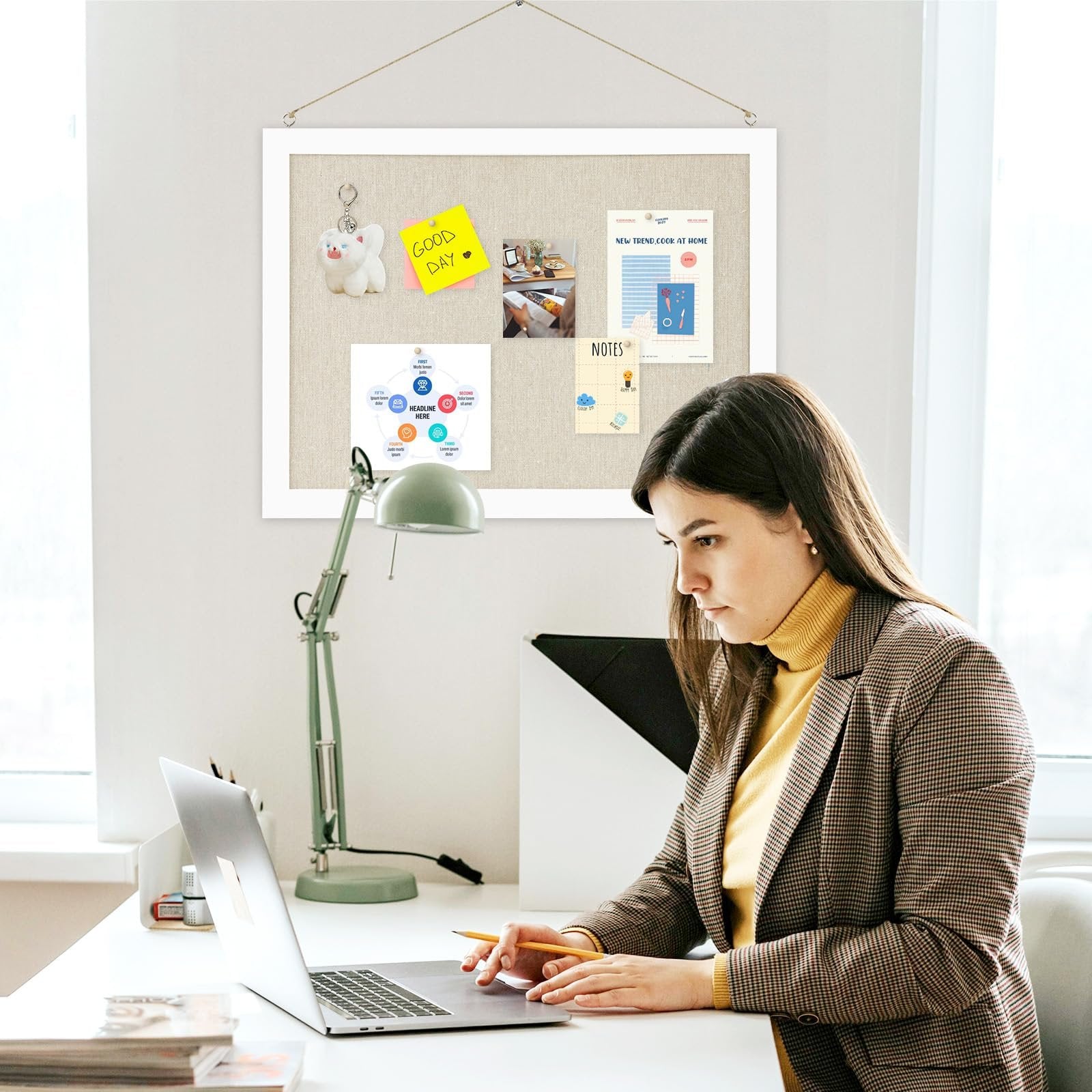 Woman working at a desk with a bulletin board displaying notes and graphics behind her