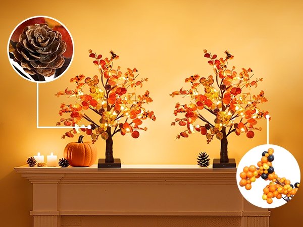 Two prelit tabletop trees with warm LEDs, eucalyptus leaves, pine cones, and berries on a mantelpiece with a pumpkin and candles.