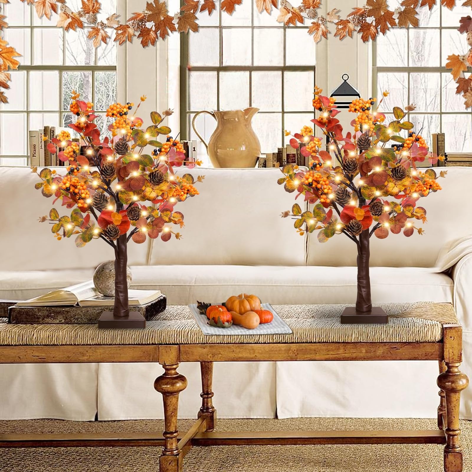 Two prelit fall tabletop trees with warm LEDs, eucalyptus leaves, pine cones, and berries on a coffee table.