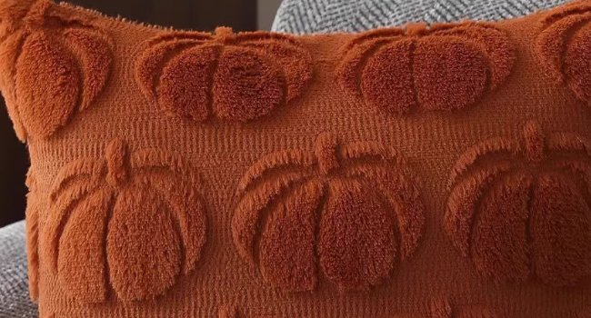Close-up of a rust orange throw pillow cover with embossed pumpkin designs and a textured faux fur finish.