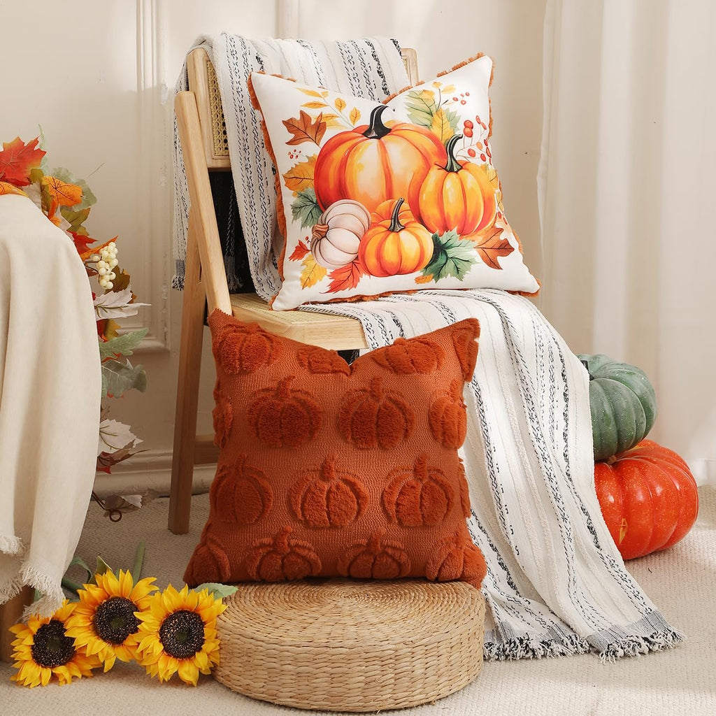 Two fall-themed throw pillows with pumpkins on a chair with a blanket and sunflowers