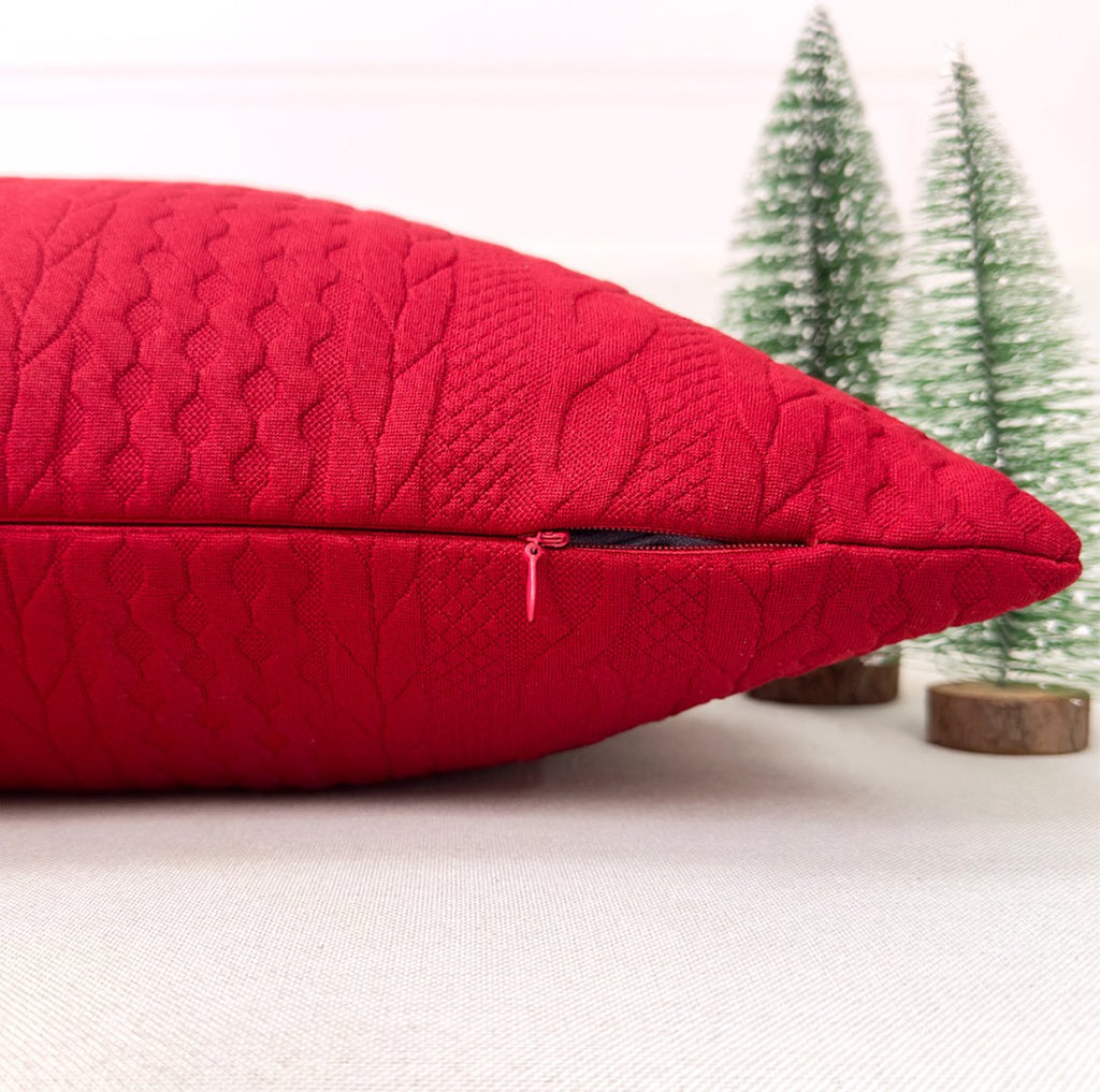 Red Christmas pillow cover with embossed knit texture and visible zipper, with miniature trees in background