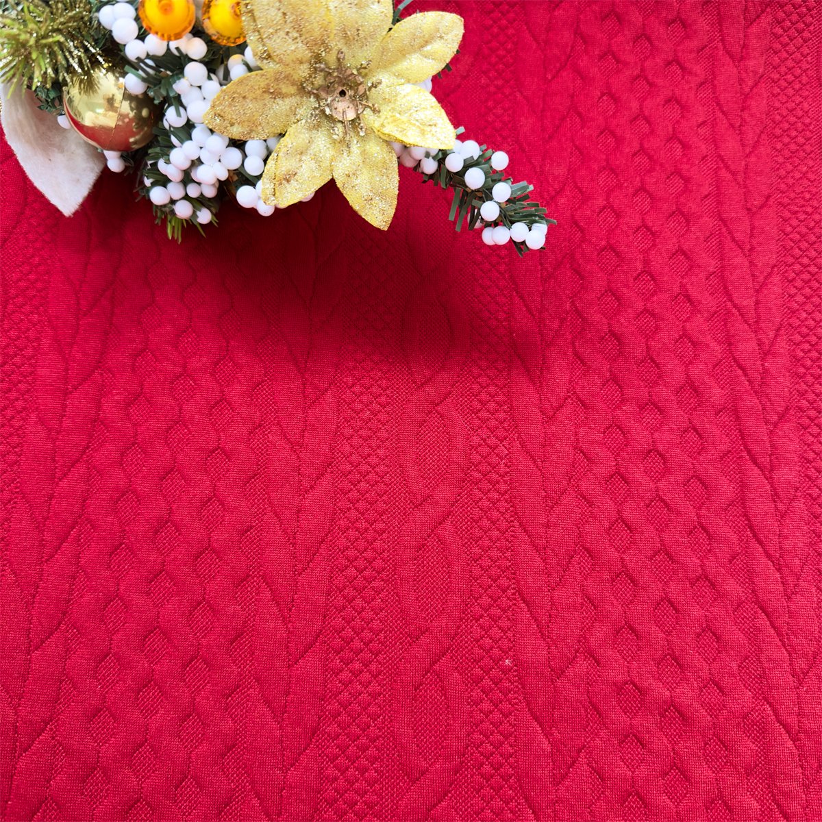 Red Christmas pillow cover with embossed knit texture and festive holiday garland in the upper left corner.